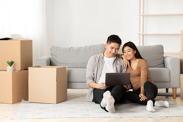 Couple sitting on floor of new home while smiling at their laptop